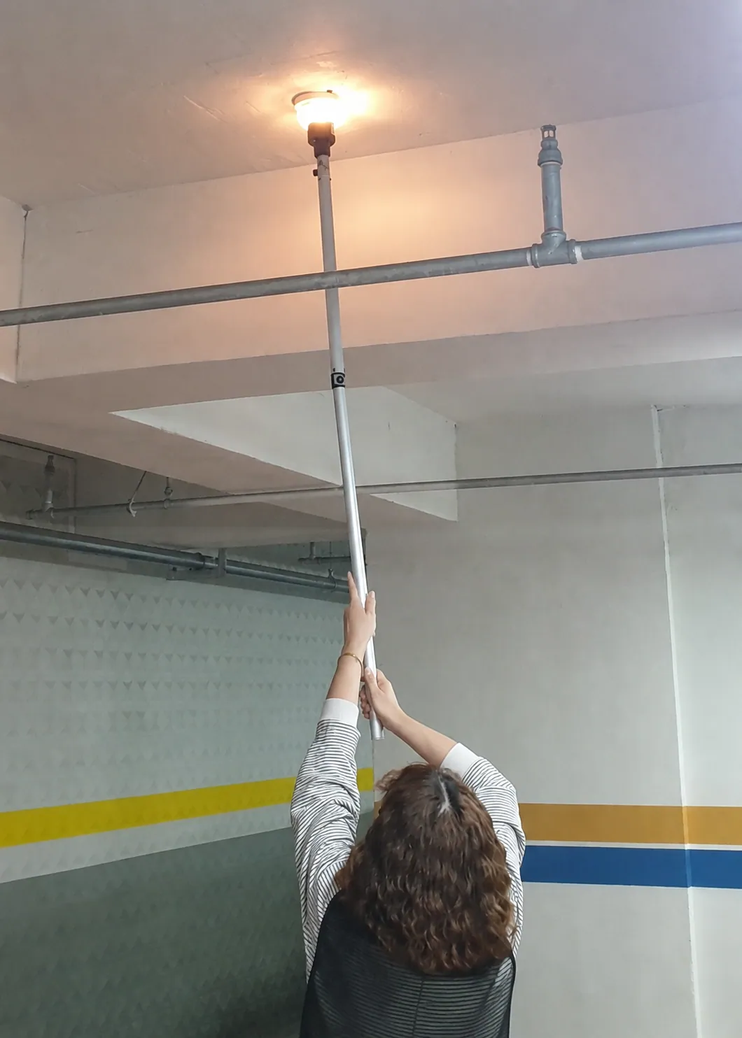 주차장 천장 화재감지기를 시험 장비로 점검하는 작업자